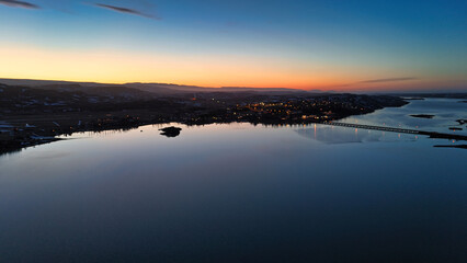 Obraz premium Beautiful yellow orange reddish sunset at dusk stretching over a lake in which slight reflections are visible