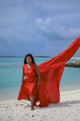 Lady in red satin flying dress flowing at the beach