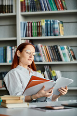 A redheaded woman engrossed in a book in a library, embraced by the solitude of her reading.