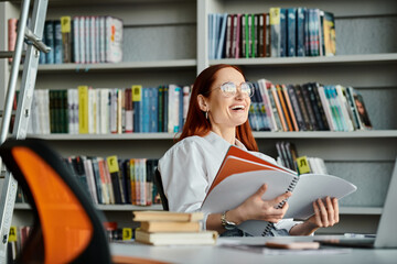 A redhead female tutor teaches online, seated at a library desk engrossed in reading a book after...