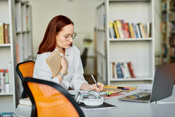 A female tutor with red hair providing an after-school lesson online, using a laptop at a desk in a library setting.