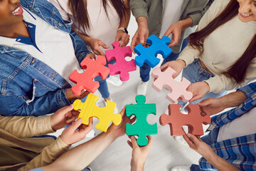A group of multiethnic young people are holding large colored puzzles in their hands, close-up, top...