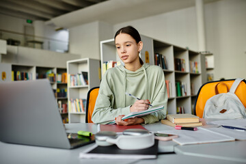 A teenage girl engrossed in her studies, typing on a laptop while sitting at a desk in a quiet...