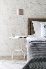 Nightstand with cup of morning coffee close to comfort bed in classic style bedroom