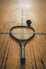 A tennis racket lying on a wooden floor, suitable for use in sports or fitness photography