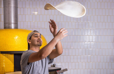 Chef tosses the pizza dough into the air. Hands of a male chef with thin round pizza dough in the...