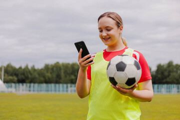 Naklejka premium Portrait of young smiling woman football player holding soccer ball and using smartphone.