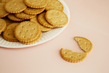 Crackers on a disposable plate and one cookie broken in half on a pink background close-up