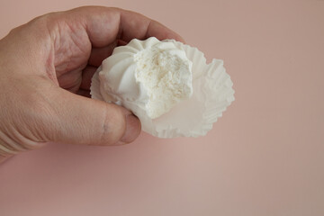 Hand holding an over-bitten marshmallow cupcake in a white paper tartlet on a pink background, delicate dessert in hand