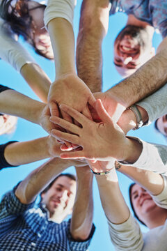 Friendship, hands and group in nature with huddle for community, solidarity or teamwork with blue sky. Low angle, unity and happy people for motivation, support or bonding together in Australia