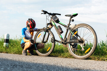 Man cyclist repairing a bike against the background of sky