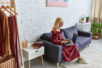 Glamorous woman in chic attire sitting on a couch, engrossed in her laptop.