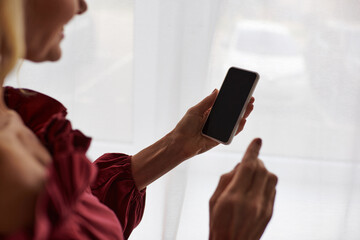 Mature woman in a red shirt stylishly holds a cell phone at home.