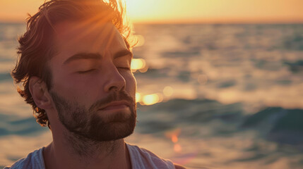 Man meditates near the ocean. The rays of the sun softly illuminate his face