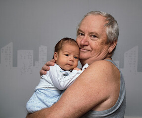 The grandfather gently holds the baby in his arms and hugs him. The grandson continues the family.