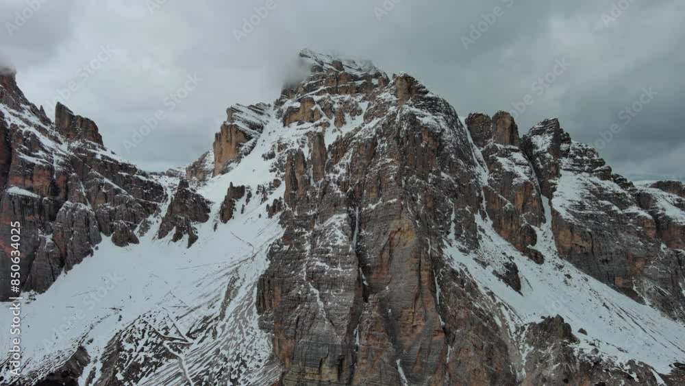 Wall mural Aerial around view of amazing rocky mountains in snow under moody gray clouds, Dolomites, Italy, 4k