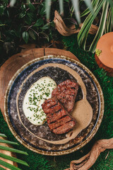 Close-up view of a luxury stone plate with grilled steak, mashed potatoes, and gravy.