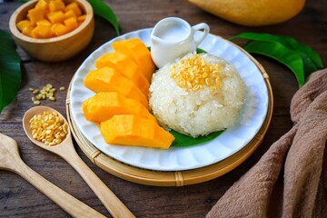 Mango and Sticky Rice on banana leaf with white plate and coconut milk wooden blackground, top view food table	