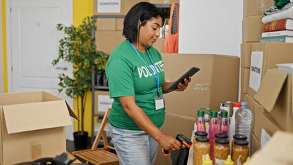 Hispanic woman volunteer sorts donations at a community center pantry indoors using tablet