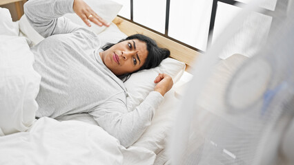 Hispanic woman feeling hot in bedroom with fan