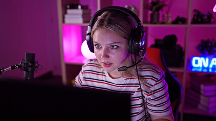 A focused young woman with headphones streams video games in a vibrant home gaming room at night.