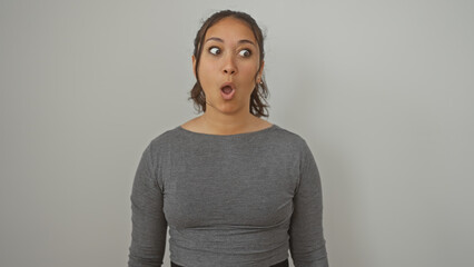 Surprised young hispanic woman with open mouth standing against a white background, portraying a reaction or emotion.