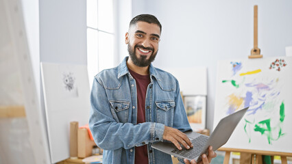 A handsome bearded man using laptop in modern art studio, radiating creativity and productivity.