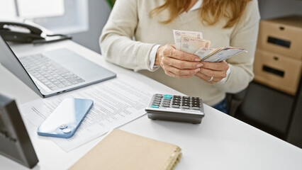 Young hispanic woman handling colombian pesos in a modern office setting.
