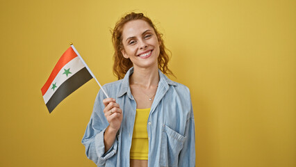 Smiling young woman holding a small syrian flag against a yellow background, exuding charm and positivity.