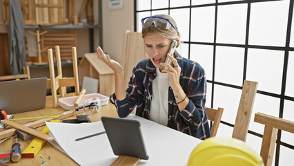 Frustrated blonde woman on a phone call in a cluttered woodworking workshop