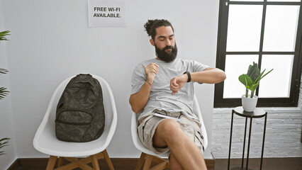 Hispanic man with beard sitting in waiting room looking at watch, indicating punctuality or wait,...