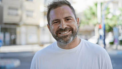 Obraz premium A smiling hispanic middle-aged man with grey hair posing outdoors on an urban street, reflecting an amiable personality.