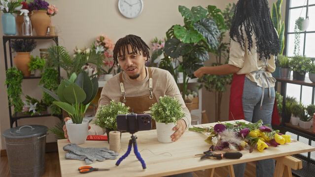Man and woman working together in a flower shop with plants, using a smartphone for recording.