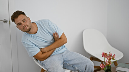 Handsome young hispanic man sitting thoughtfully in a modern white room