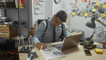 Hispanic detective taking notes at police station with evidence board in background.