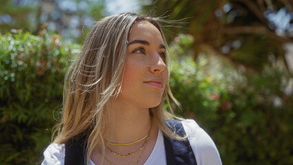 Attractive young blonde woman posing outdoors in an urban park on a sunny day, showcasing her natural beauty and casual style.