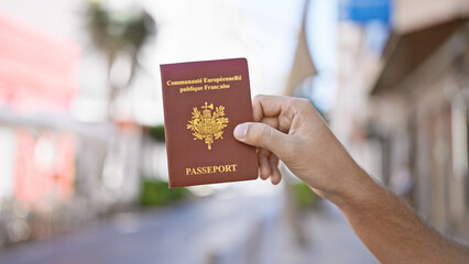 Close-up of a hand holding a french passport in an urban street setting, creating a concept of travel or identity.
