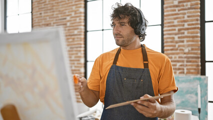 Hispanic man painting canvas in art studio wearing headphones and apron © Krakenimages.com