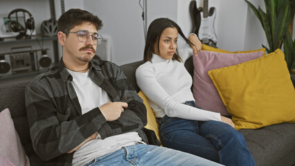 Couple in dispute sitting apart on couch, gloomy atmosphere in a modern living room interior suggests relationship issue.