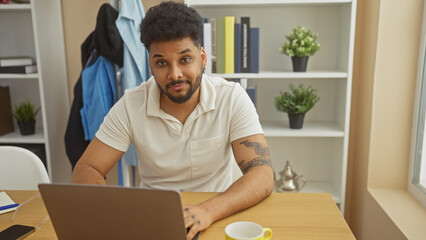 A handsome african american man works from home, sitting at a desk with a laptop in his modern...