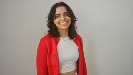 Young attractive hispanic woman in a red cardigan with a white background wall, smiling confidently...