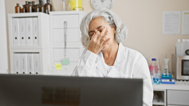 An exhausted grey-haired woman in a lab setting evokes stress or overwork.