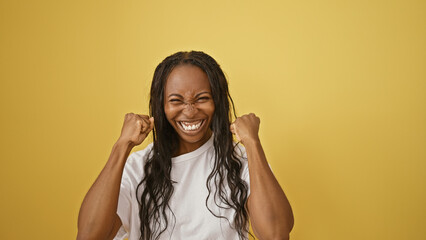 Fototapeta premium An overjoyed young woman with curly hair celebrates excitedly against a yellow background.