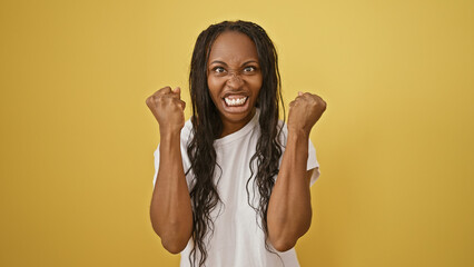 Angry young african american woman clenching fists against a yellow isolated background