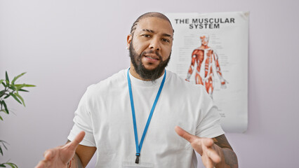 Handsome black man with beard wearing lanyard in a clinic with muscular system poster behind him