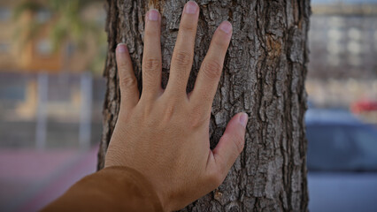 A man's hand touching the rough texture of a tree trunk outdoors symbolizes human connection with nature.