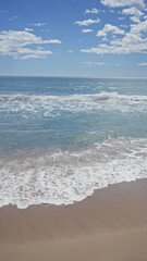 Tranquil beach scene with clear skies, sparkling sea, white foam, and pristine sand conveying serenity and leisure.