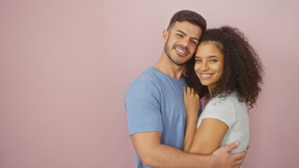 Affectionate man and woman hugging, smiling against a plain pink background, depicting love and...