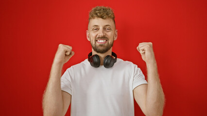 A joyful young man with a beard and headphones celebrates against a red background.