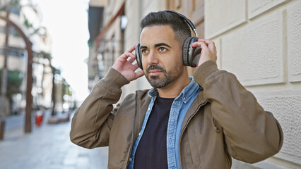 Handsome bearded hispanic man listens to music with headphones on a city street.